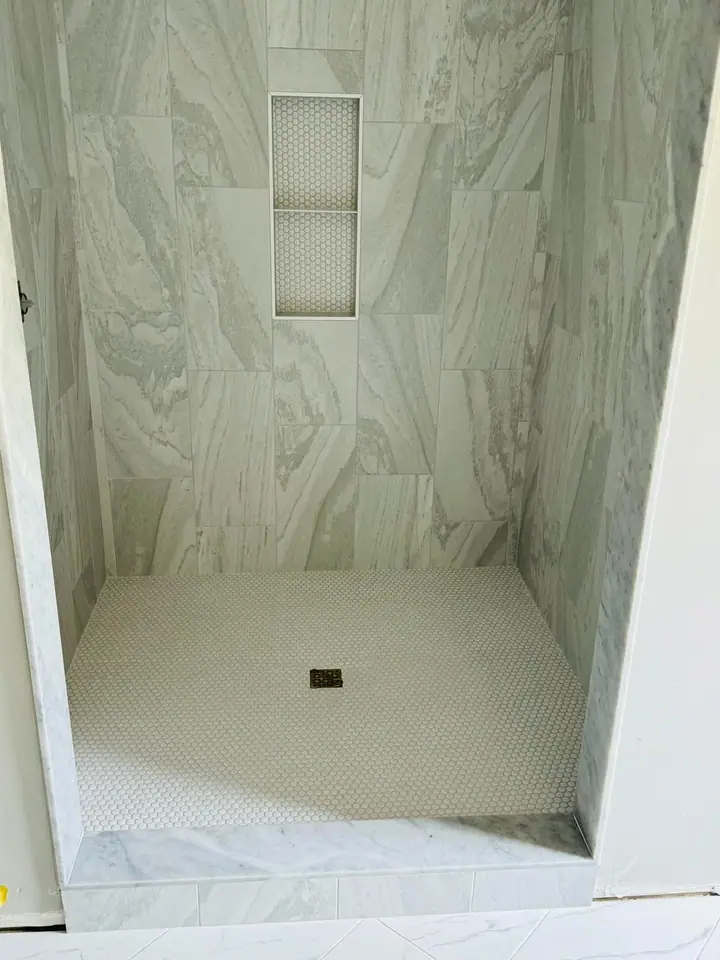 Walk-in shower with marble-look walls and a white penny mosaic floor