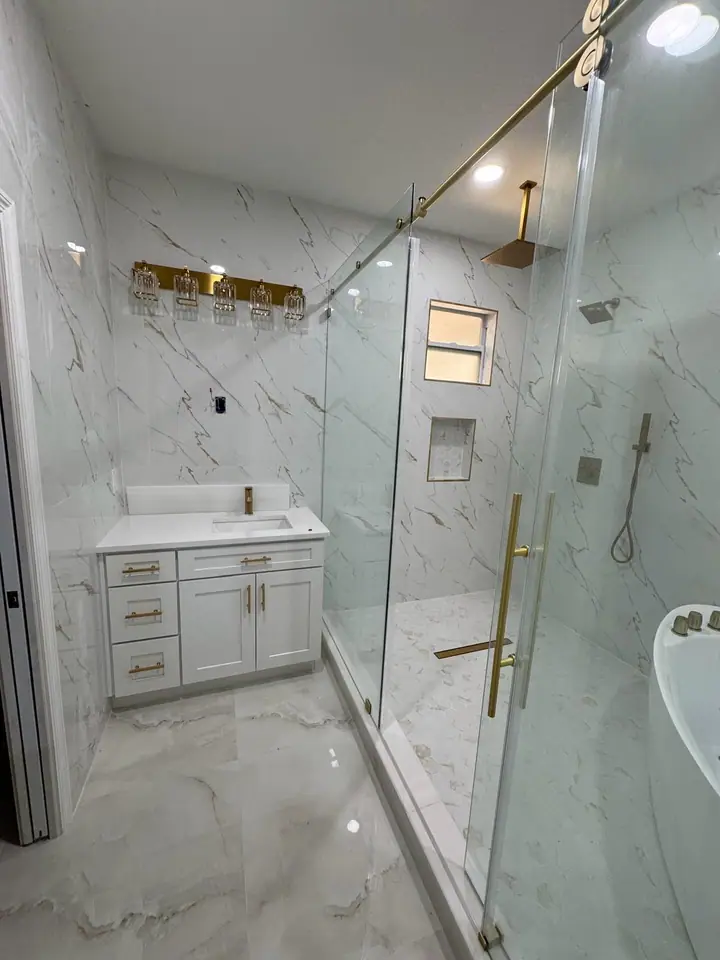 Luxury bathroom with marble-look tile, gold fixtures, and a glass shower
