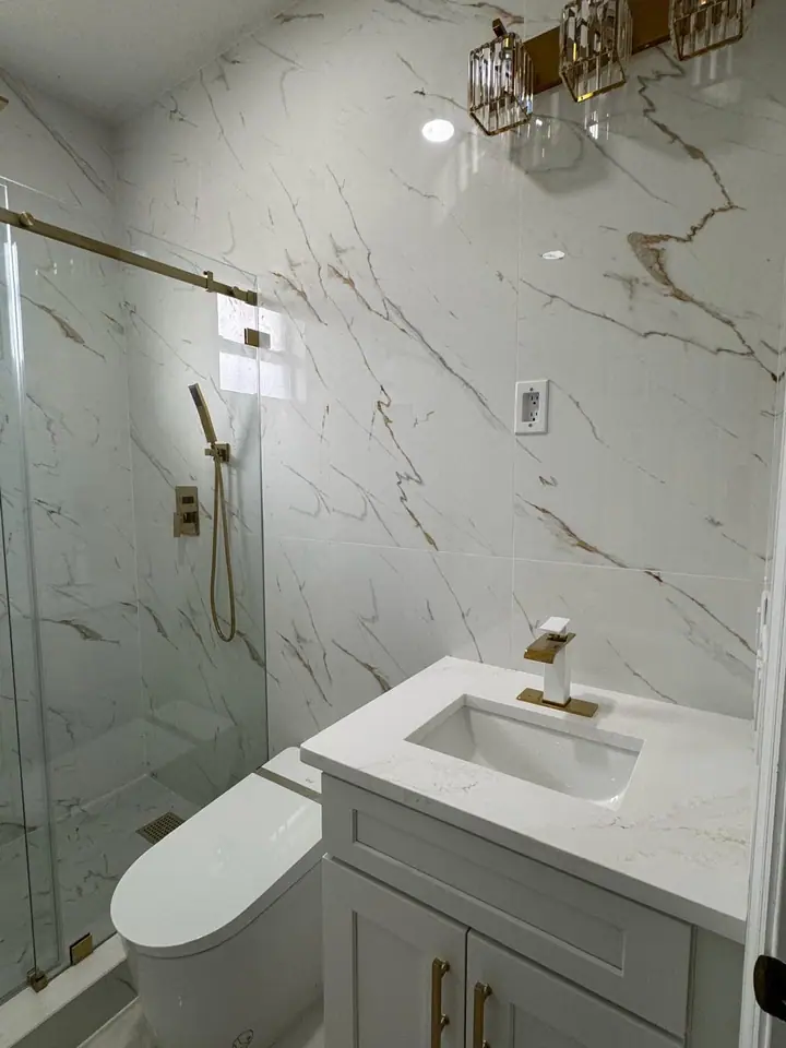 Luxury bathroom with marble-look tile, gold fixtures, and a glass shower