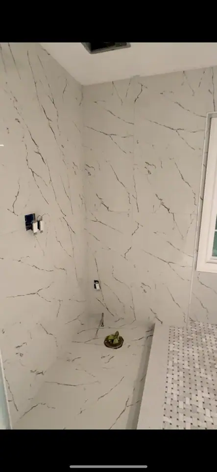 Walk-in shower with marble walls, mosaic floor, and a tiled corner bench