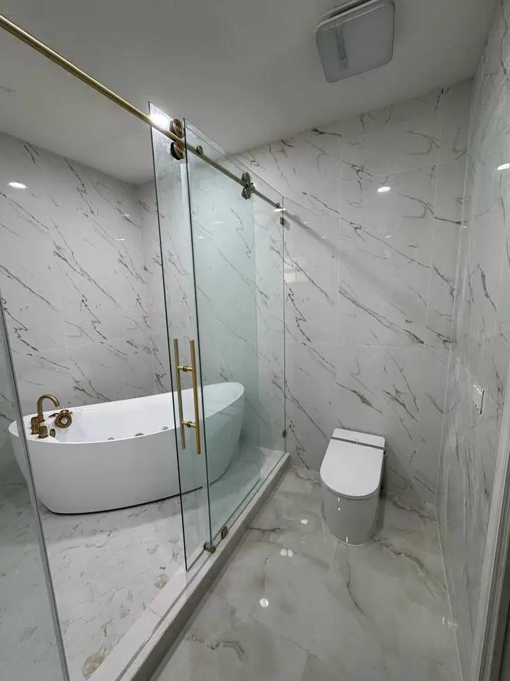 Luxury bathroom with marble-look tile, gold fixtures, and a glass shower