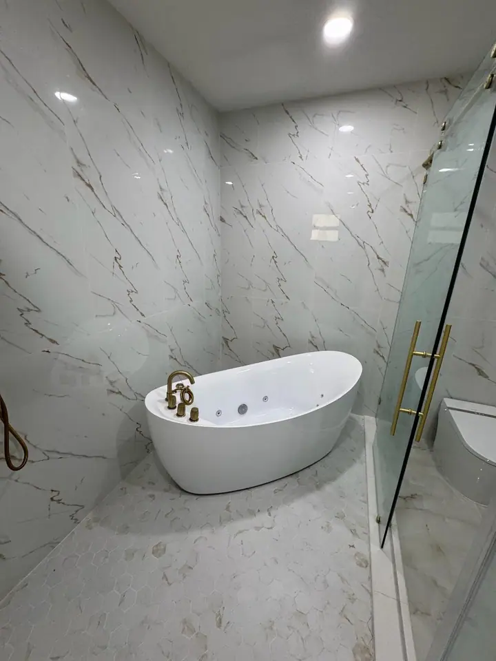 Luxury bathroom with marble-look tile, gold fixtures, and a glass shower