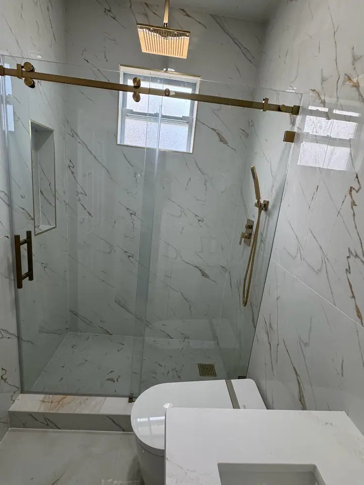 Luxury bathroom with marble-look tile, gold fixtures, and a glass shower